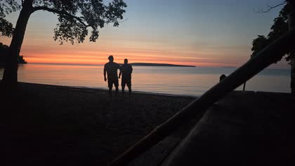 Two people silhouetted against a sunset on a Lake Superior beach